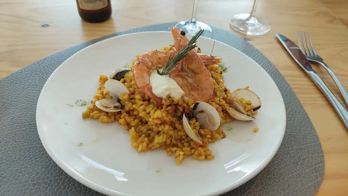 Plato de arroz amarillo con almejas y dos gambones coronados con alioli y una rama de romero