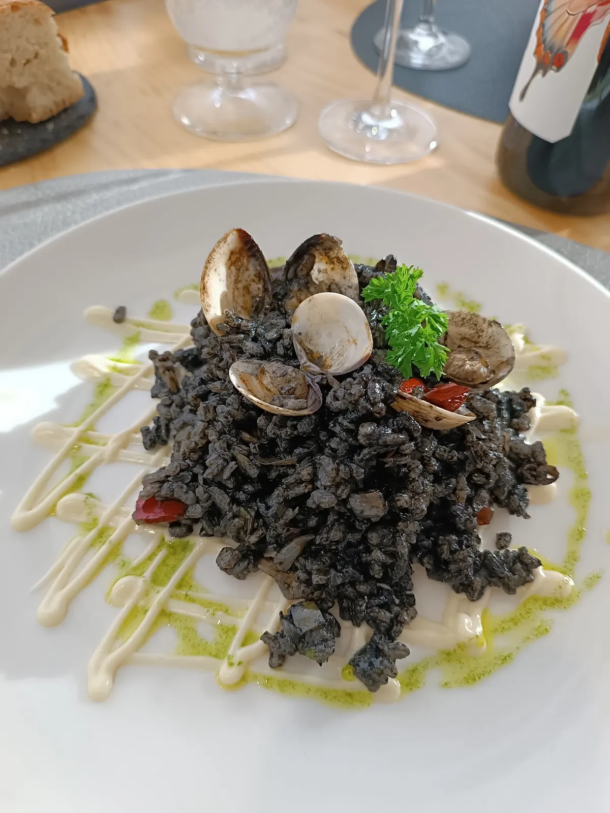 Arroz negro con almejas y perejil sobre trazos de alioli y aceite verde en un plato blanco