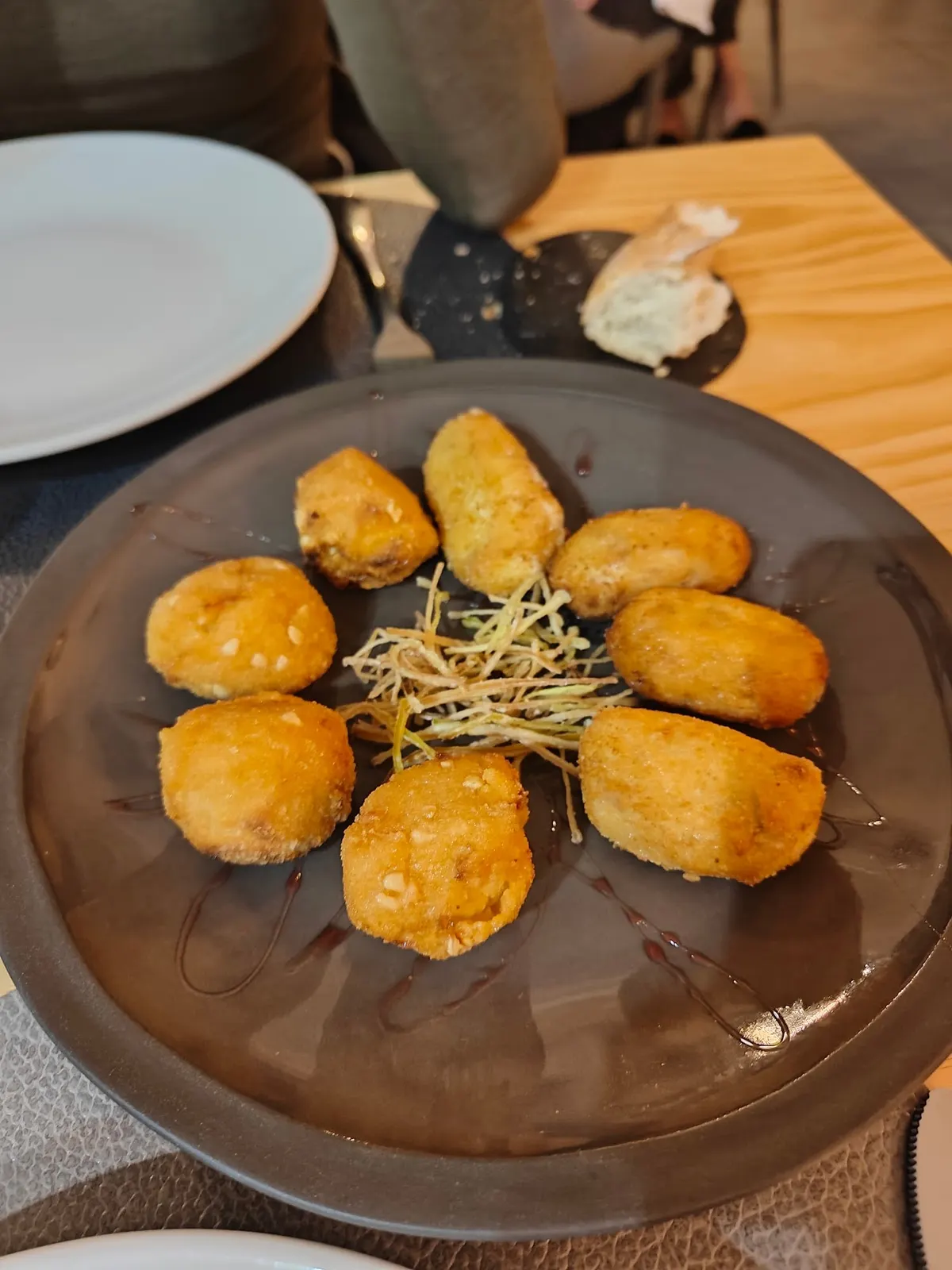 Croquetas doradas con patata paja en un plato de barro oscuro