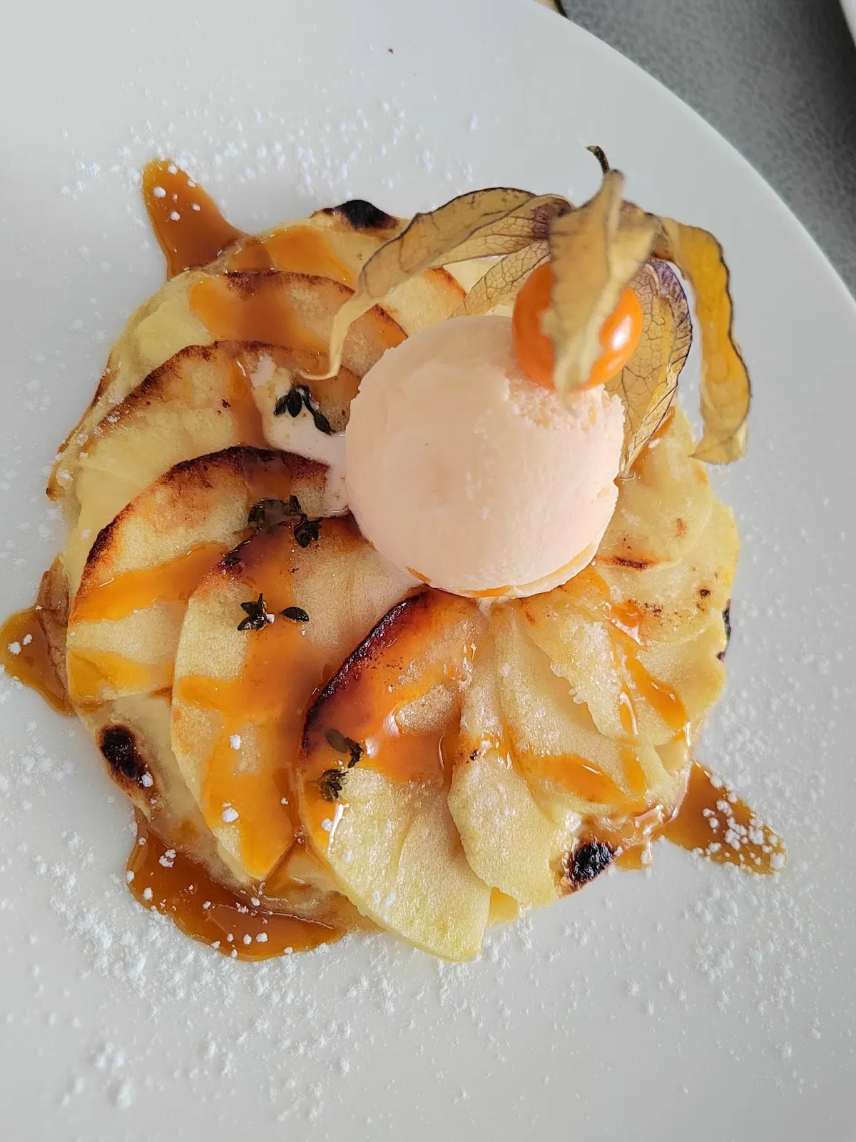 Láminas de manzana caramelizada en abanico con tomillo, una bola de helado y una physalis
